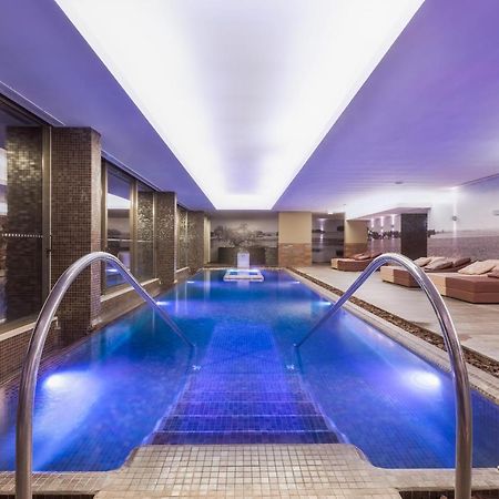 Ap Lago Montargil - Conference & Spa Dış mekan fotoğraf The photo shows a modern indoor swimming pool area. The pool features a sleek design with steps leading into the water and a gentle curve at the sides. The water is illuminated in a blue hue, enhancing the relaxing atmosphere. Surrounding the pool ar