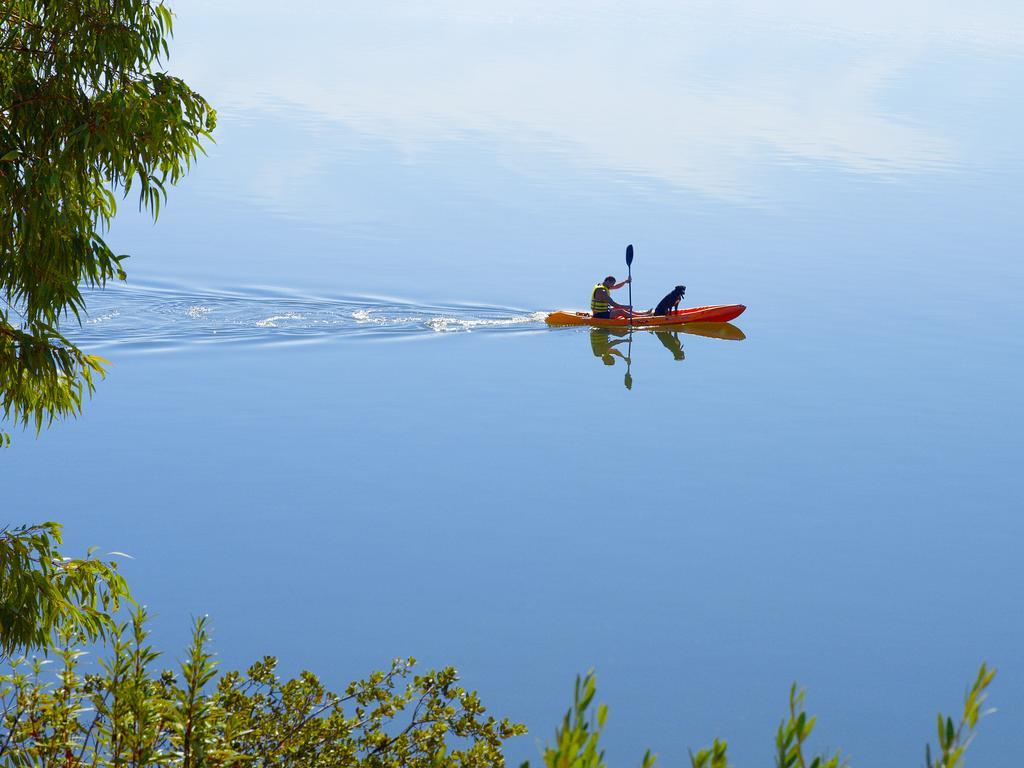 Ap Lago Montargil - Conference & Spa Dış mekan fotoğraf The photo shows a serene scene of a person kayaking on a calm body of water. The surface of the water is very smooth, reflecting the surroundings, and there is a gentle wake behind the kayak indicating movement. The kayaker is wearing a life jacket a