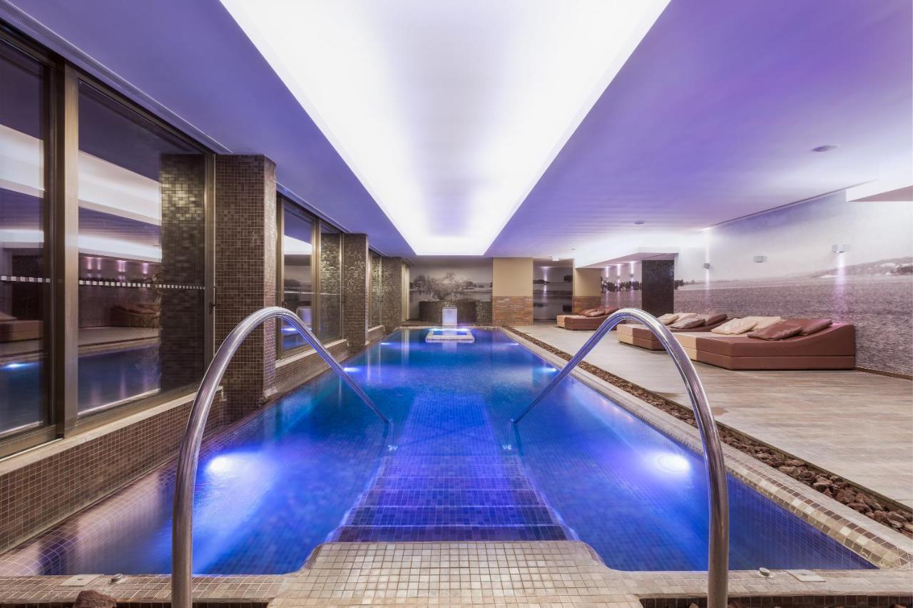 Ap Lago Montargil - Conference & Spa Dış mekan fotoğraf The photo shows a modern indoor swimming pool area. The pool features a sleek design with steps leading into the water and a gentle curve at the sides. The water is illuminated in a blue hue, enhancing the relaxing atmosphere. Surrounding the pool ar