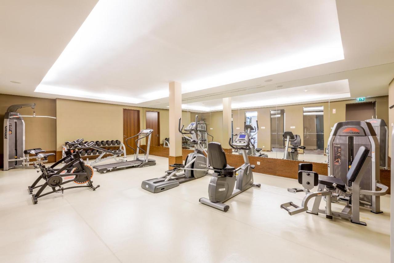 Ap Lago Montargil - Conference & Spa Dış mekan fotoğraf The image shows a modern gym interior featuring various exercise equipment. On the left, there are free weights and weight benches. In the center, there are multiple machines, including a stationary bike and an elliptical. The space is well-lit with 
