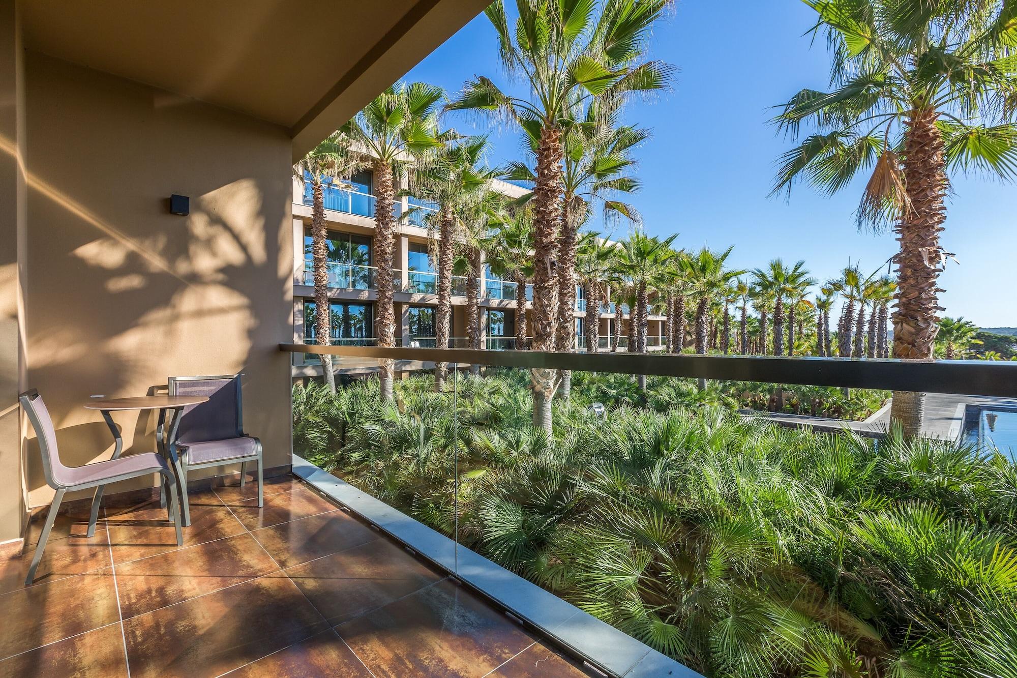 Ap Lago Montargil - Conference & Spa Dış mekan fotoğraf The photo shows a balcony with modern furniture, including a chair and a small table. In the background, there are tall palm trees and lush greenery, suggesting a tropical or resort-like setting. The buildings in the distance are likely part of a hot