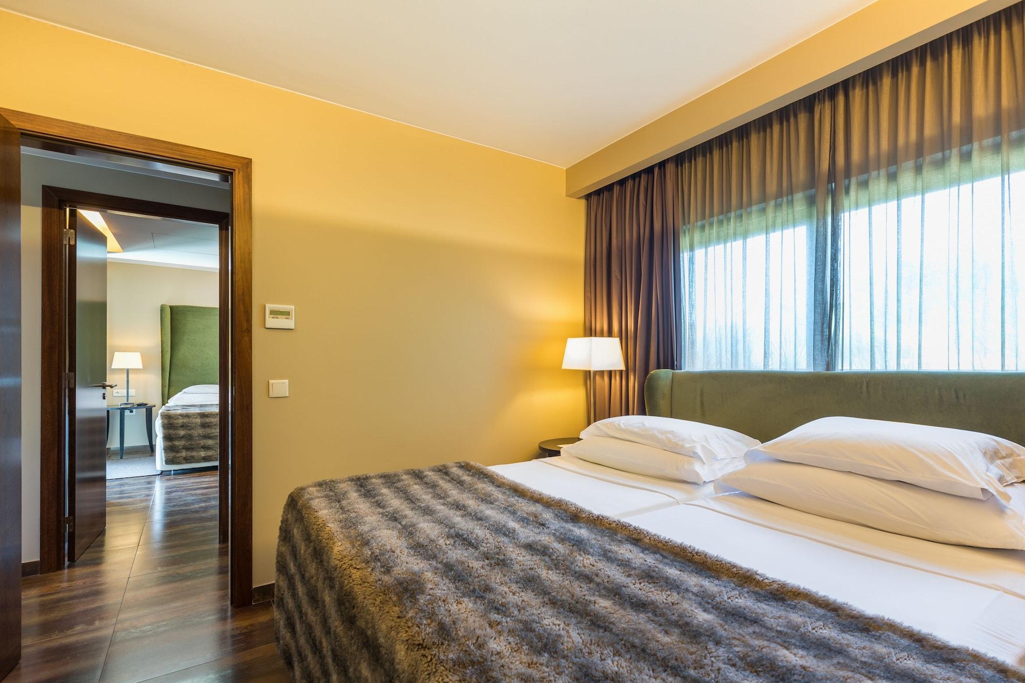 Ap Lago Montargil - Conference & Spa Dış mekan fotoğraf The photo shows the interior of a well-furnished hotel room. It features two beds with white linens and a gray decorative throw on top. The walls are painted a warm yellow, and there are floor-to-ceiling windows covered with dark curtains that allow 