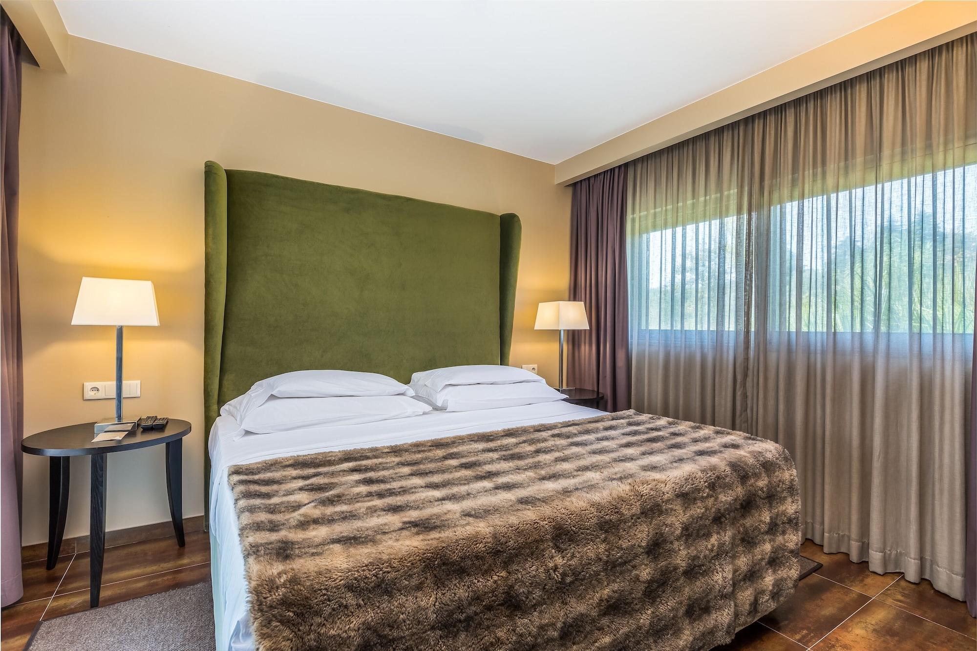 Ap Lago Montargil - Conference & Spa Dış mekan fotoğraf The photo shows a cozy hotel room featuring a large bed with two white pillows and a fur-style blanket draped over it. Behind the bed is a tall, green headboard that adds a touch of color to the room. On either side of the bed are bedside tables, eac