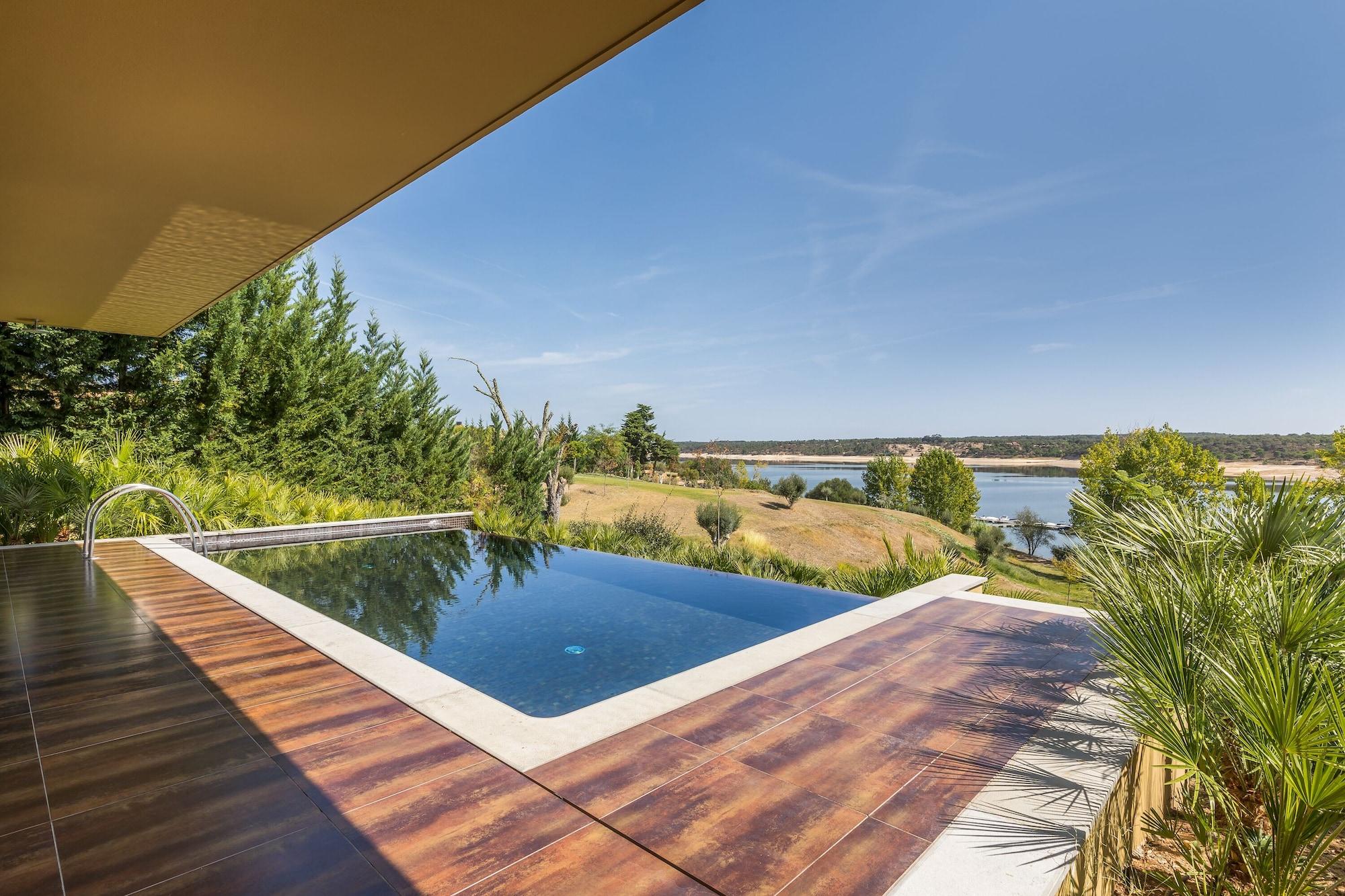 Ap Lago Montargil - Conference & Spa Dış mekan fotoğraf The photo shows a luxurious infinity pool situated on a terrace or deck. The pool features a sleek, modern design with a dark blue surface that reflects the surrounding scenery. In the background, there is a landscape of rolling hills and a body of w