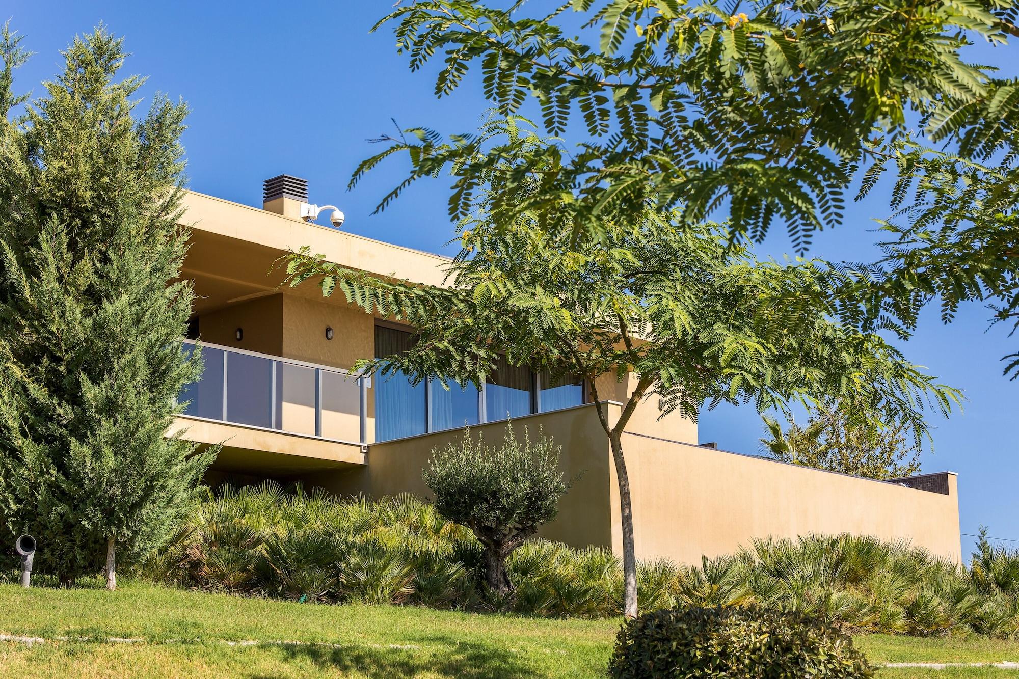 Ap Lago Montargil - Conference & Spa Dış mekan fotoğraf The photo showcases a modern house situated on a grassy slope. The house features a light-colored exterior with large windows and a balcony. Surrounding the building are several trees and landscaping that enhances the natural environment. The sky is 