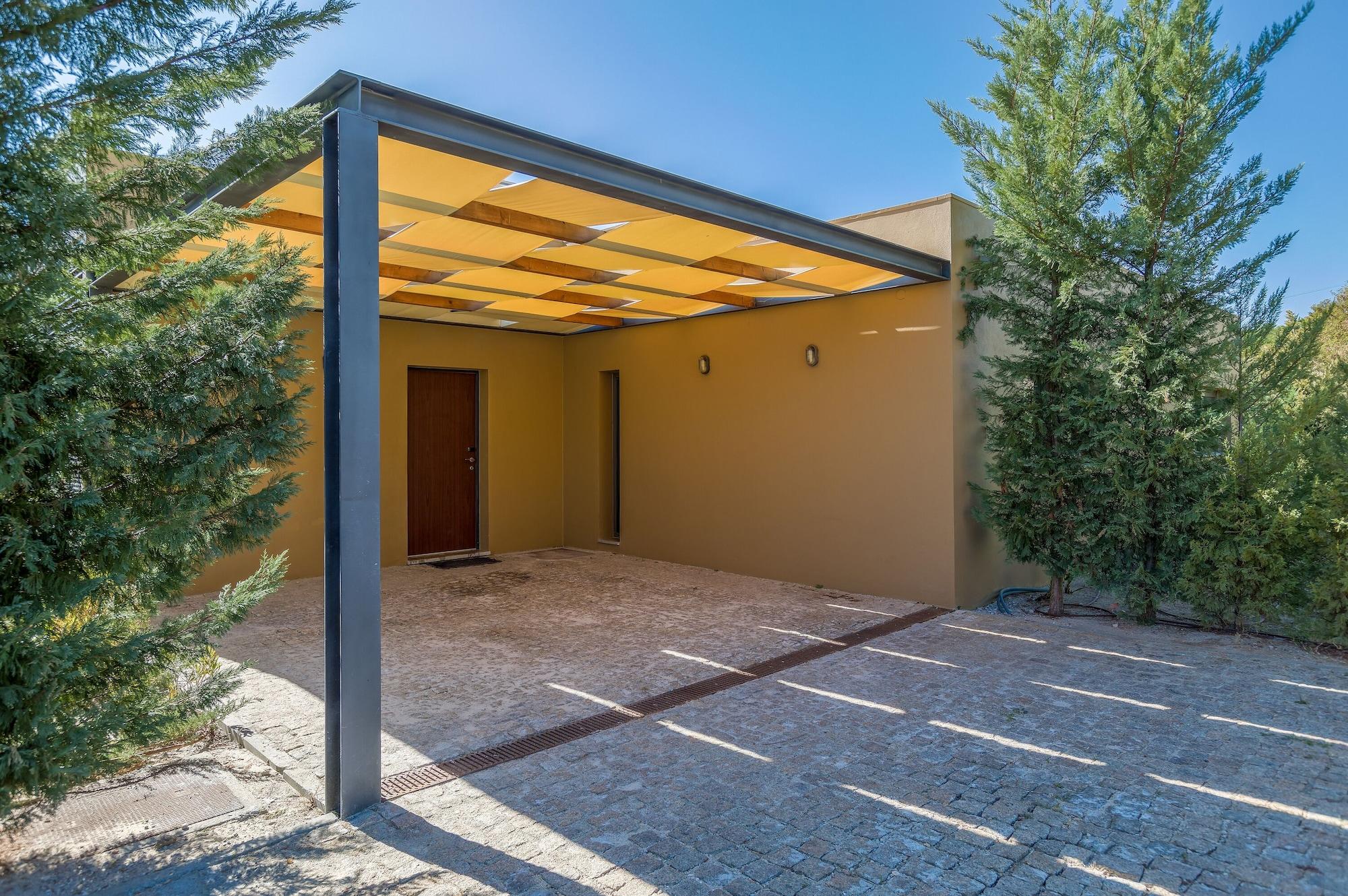 Ap Lago Montargil - Conference & Spa Dış mekan fotoğraf The photo shows an exterior view of a modern structure with a carport. The carport has a sleek, metallic frame and a yellowish canopy above it. In front of the structure, there is a paved area made of stone or tiles. The main entrance features a wood