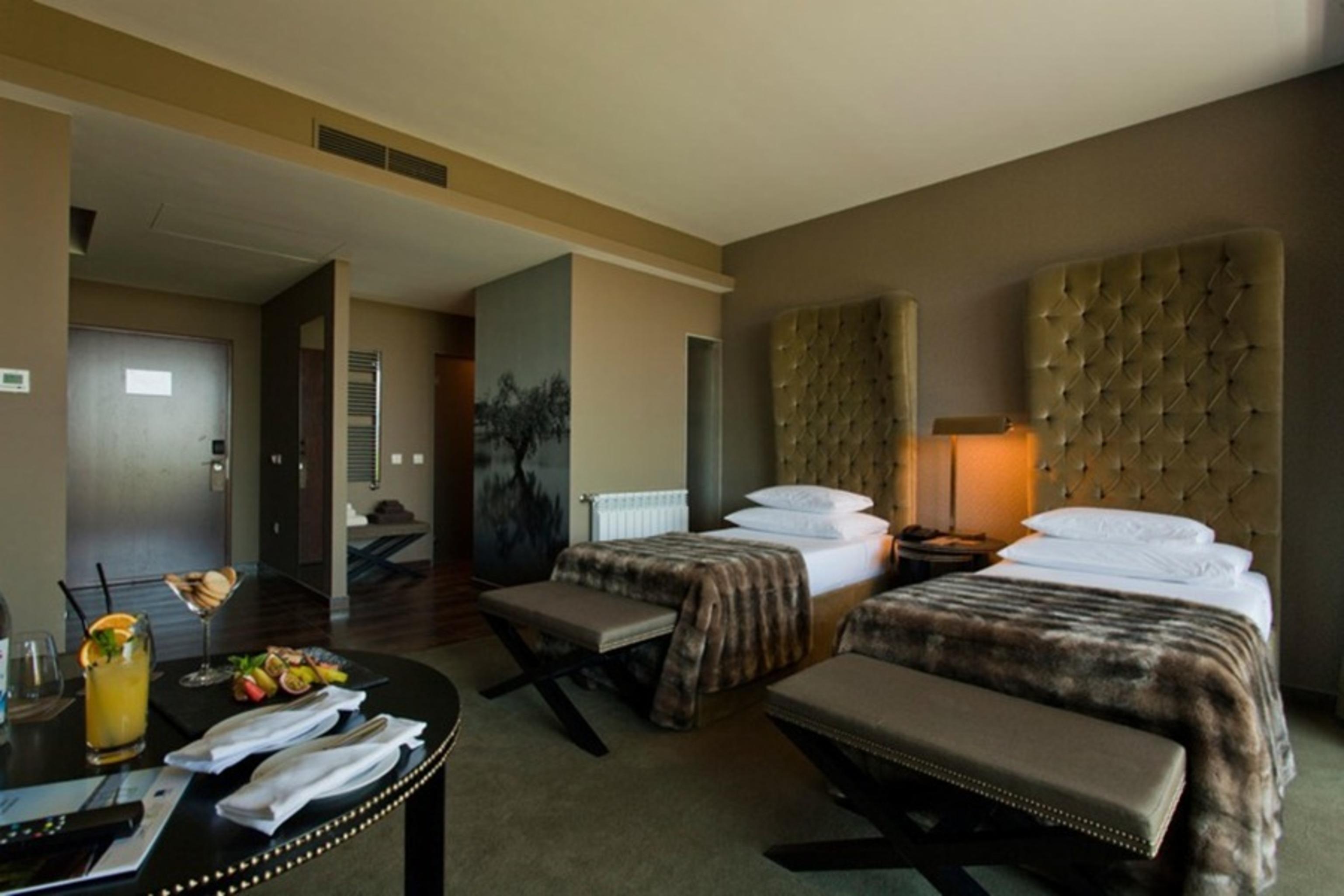 Ap Lago Montargil - Conference & Spa Dış mekan fotoğraf The photo shows a stylish hotel room featuring two beds with plush, upholstered headboards. The room has a modern and elegant design, with earthy tones dominating the decor. A small round table is set up in the foreground, displaying a drink and some