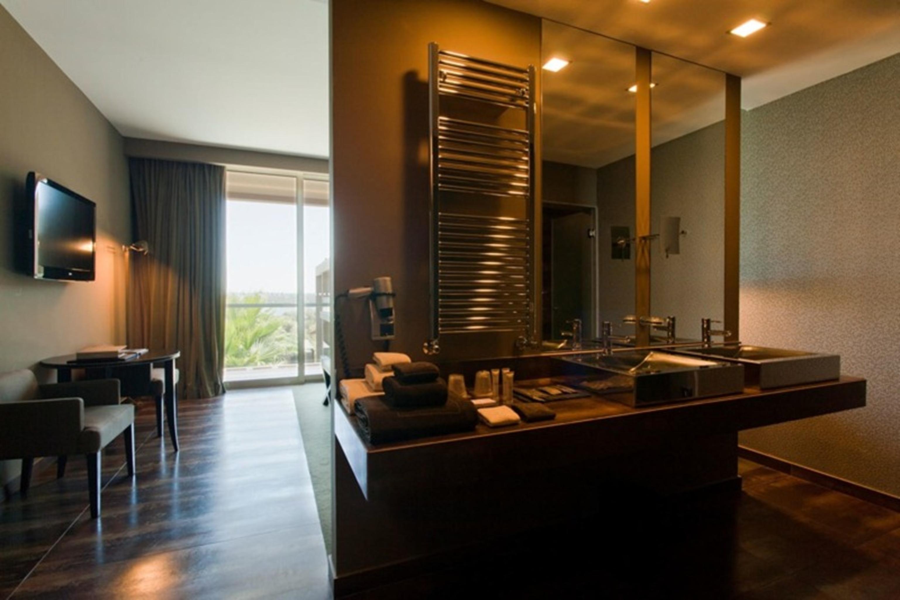 Ap Lago Montargil - Conference & Spa Dış mekan fotoğraf The photo displays a modern hotel room with a contemporary design. The room features a large window, allowing natural light to enter and offering a view outside. On one side, there is a sitting area with a small table and chairs. The other side showc