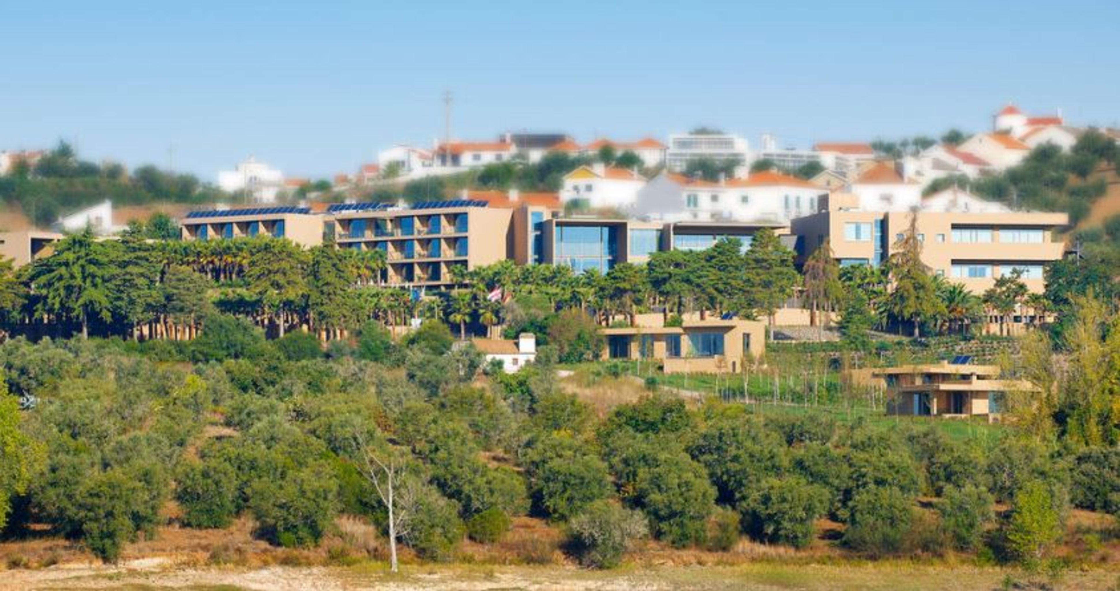 Ap Lago Montargil - Conference & Spa Dış mekan fotoğraf The photo shows a hillside view of a modern resort or hotel complex surrounded by greenery. The buildings are designed with a blend of contemporary architecture and natural elements, featuring wooden accents, large windows, and terraces. In the backg