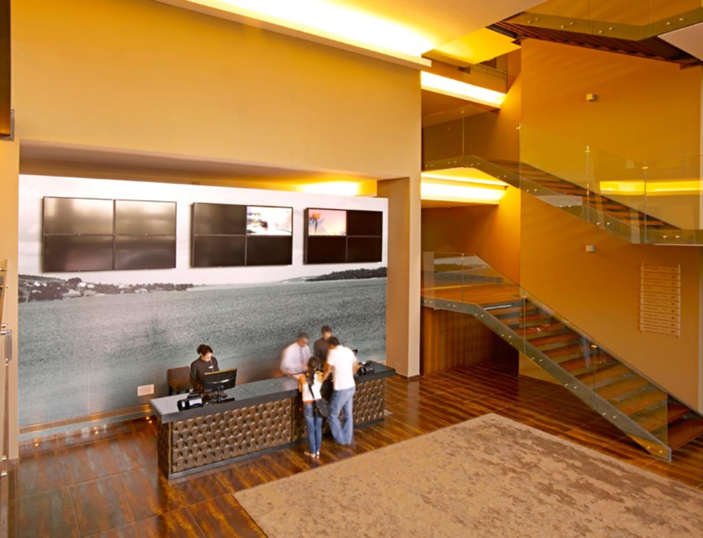 Ap Lago Montargil - Conference & Spa Dış mekan fotoğraf The photo depicts a modern lobby area with a reception desk. The design features a combination of warm colors and wood flooring. In the background, there is a large wall-mounted screen or display, showcasing several monitors. The wall behind the desk