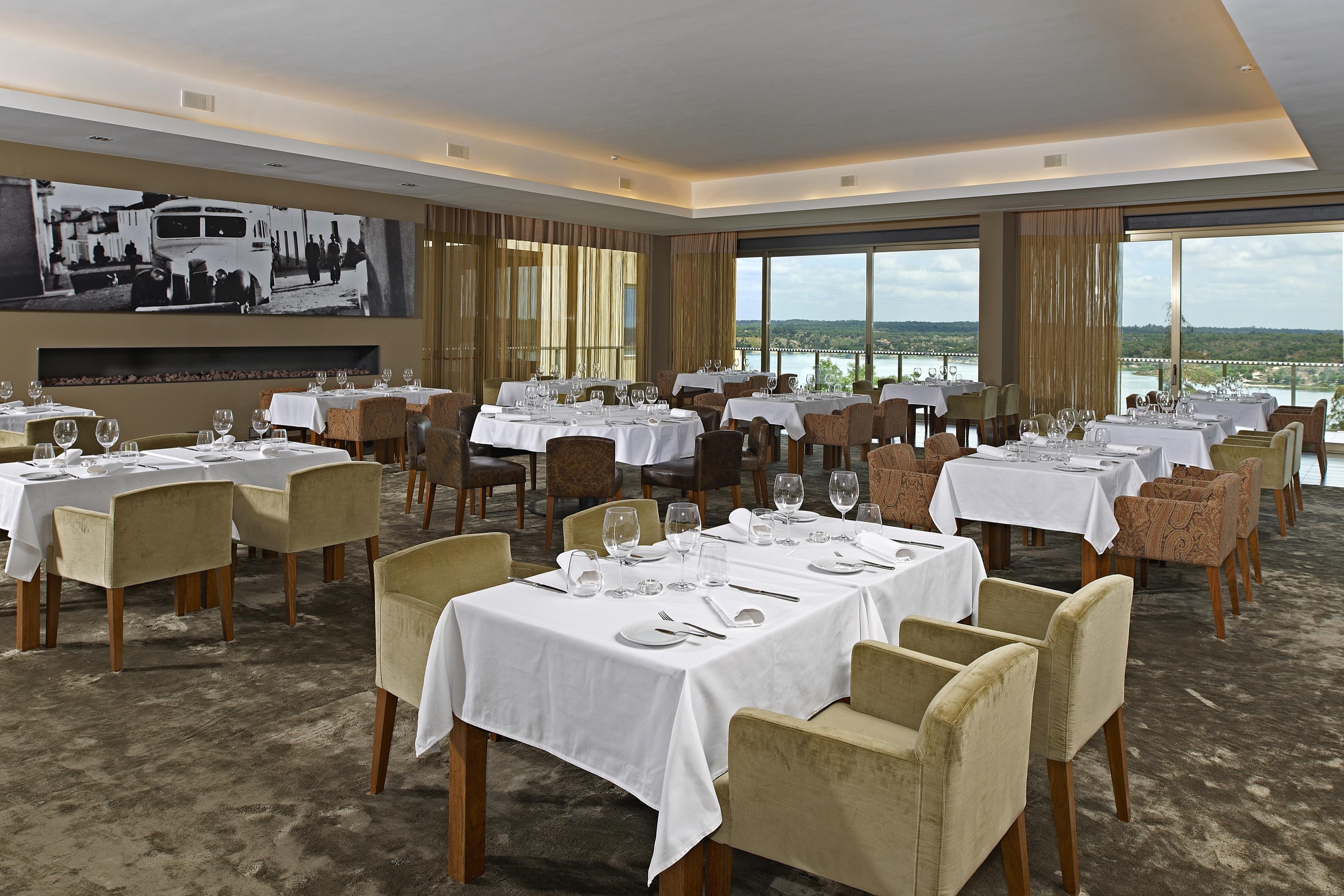Ap Lago Montargil - Conference & Spa Dış mekan fotoğraf The photo shows an elegant restaurant interior featuring neatly arranged tables with white tablecloths. Each table is set with plates, cutlery, and glasses. The seating includes a mix of upholstered chairs in different colors—some light and others da