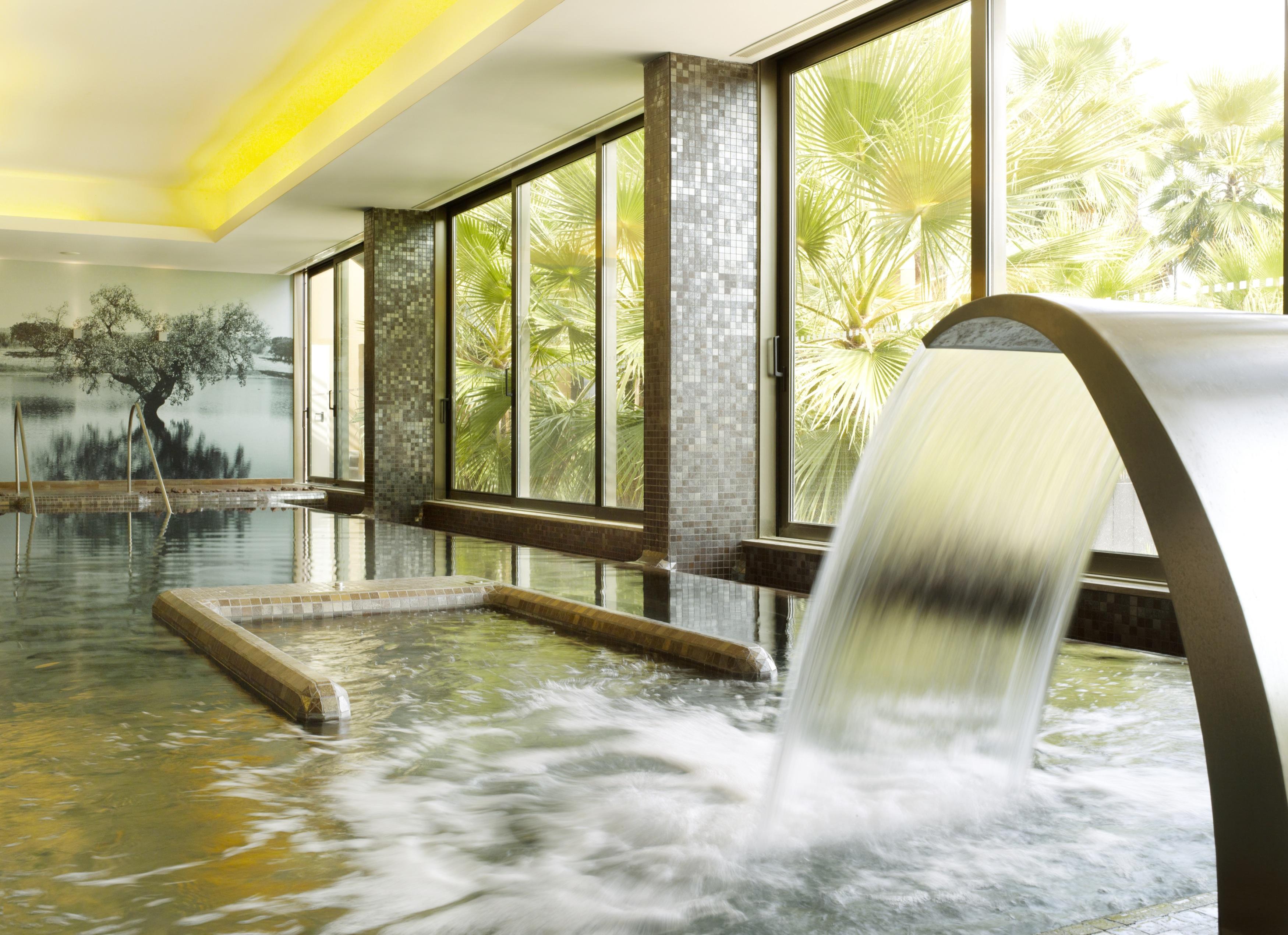 Ap Lago Montargil - Conference & Spa Dış mekan fotoğraf The photo depicts a serene spa environment featuring a tranquil indoor pool area. There is a sleek, modern water feature that spills water gracefully into the pool. Large windows allow natural light to flood the space, showcasing views of lush greene
