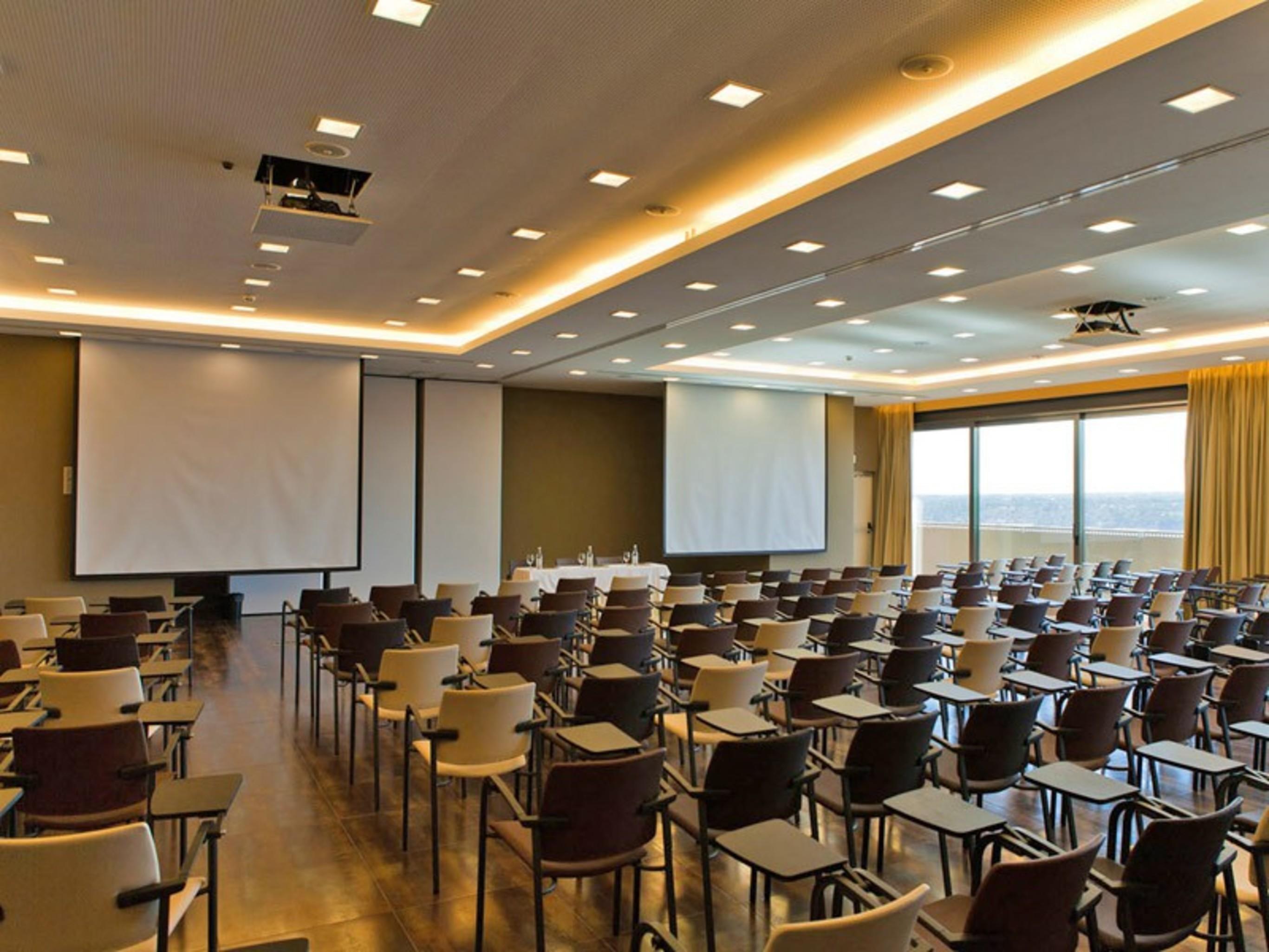 Ap Lago Montargil - Conference & Spa Dış mekan fotoğraf The photo shows a large conference room set up for a presentation or meeting. There are multiple rows of chairs arranged in a semi-theater style, facing two large projection screens. The room has a modern design, with soft lighting and large windows 